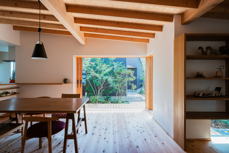 鎌ケ谷市「鎌ケ谷の家D」　木製全開サッシを全開した状態　窓の外に緑が見える　化粧垂木と漆喰の部屋