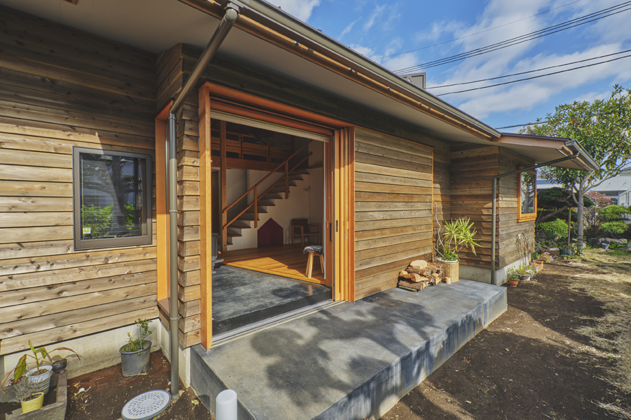 伊勢原市の平屋「私の巣」土間の木製全開サッシを全開した状態の外観　墨入りモルタルのテラスに繋がる