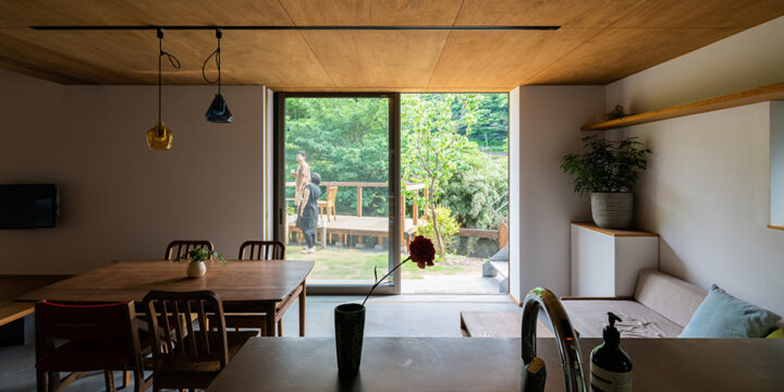 葉山「土間から四季を、呼吸する家」キッチンから土間のダイニング越しに緑豊かな庭を見ている