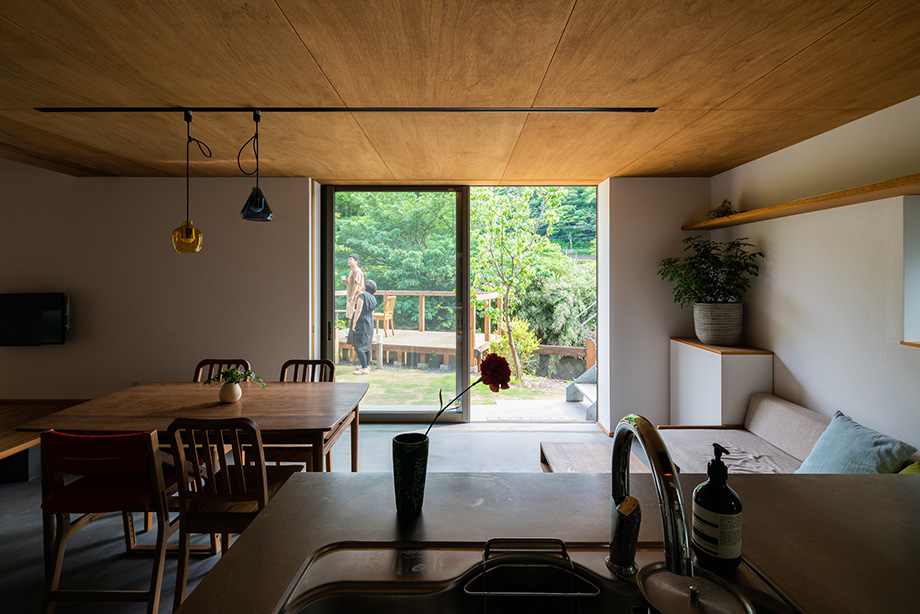 葉山「土間から四季を、呼吸する家」キッチンから土間のダイニング越しに緑豊かな庭を見ている