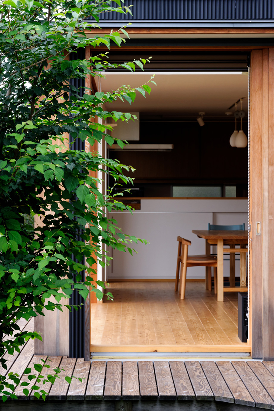 埼玉県「蓮田の家」東面の木製全開サッシを全開した状態をデッキから見ている。その奥にリビングが越しにダイニングが見えている