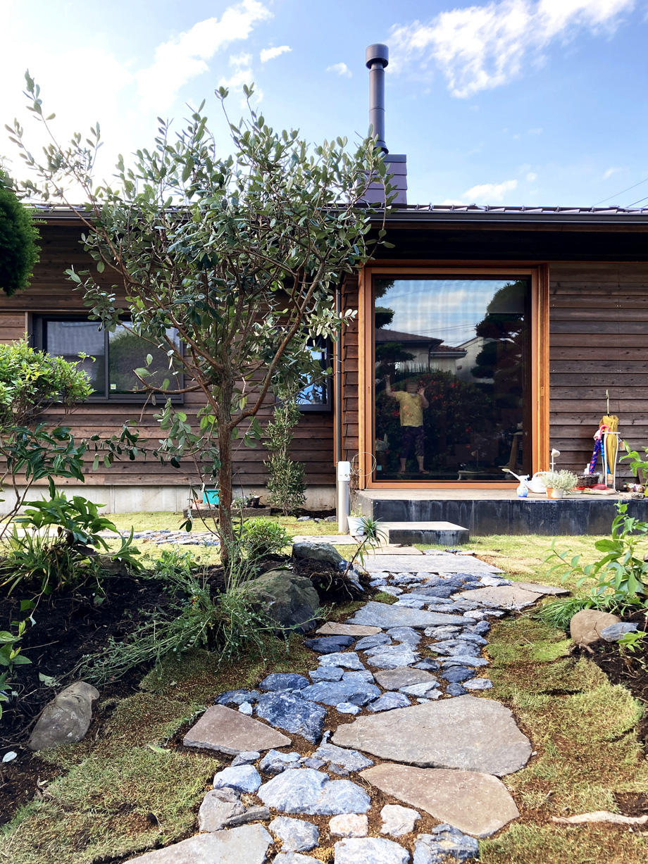 伊勢原市の平屋「私の巣」土間の木製全開サッシを閉じた状態の外観　墨入りモルタルのテラス