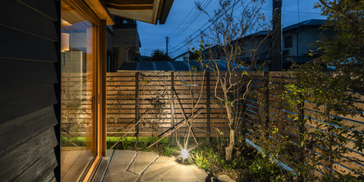 八千代市の平屋「平屋22」の木製全開サッシを閉じた状態の夕景の外観 石（鉄平石）のテラスに繋がる