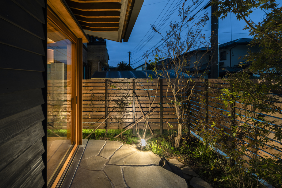 八千代市の平屋「平屋22」の木製全開サッシを閉じた状態の夕景の外観
石（鉄平石）のテラスに繋がる