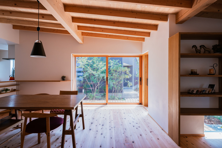 鎌ケ谷市「鎌ケ谷の家D」　木製全開サッシを閉じた状態　窓の外に緑が見える　化粧垂木と漆喰の部屋