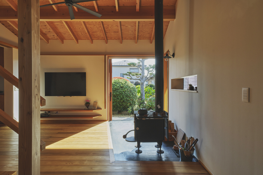 伊勢原市の平屋「私の巣」土間の木製全開サッシを全開した状態を室内の土間から見ている　土間には薪ストーブがある　天井は化粧垂木